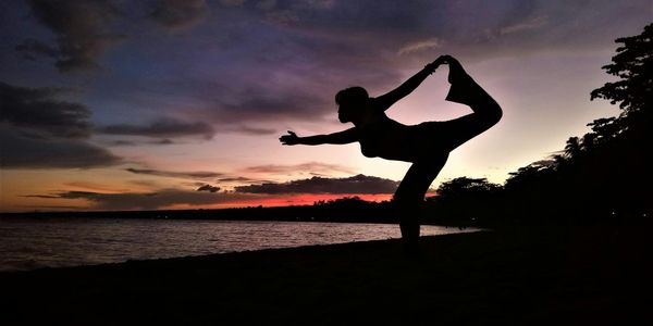 Silhouette of a person in a balancing yoga posture at sunset.